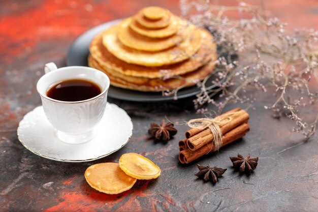 Nahaufnahme des leckeren Frühstücks mit plüschigen Pfannkuchen und einer Tasse Tee neben Zimtkalk