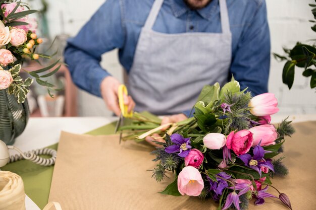 Nahaufnahme des männlichen Floristen das Papier für die Verpackung des Blumenblumenstraußes schneiden