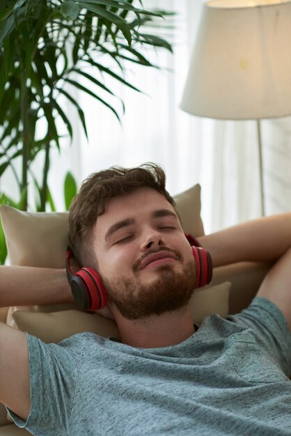 Nahaufnahme des Mannes Musik genießend, die auf Couchhänden hinter seinem Kopf liegt