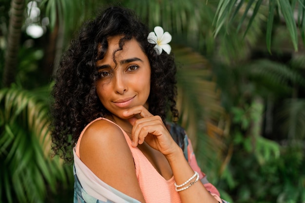 Nahaufnahme des Porträts einer glückseligen Frau mit Plumeria-Blume in den Haaren nach dem Spa im Luxusresort mit tropischem Boho-Outfit