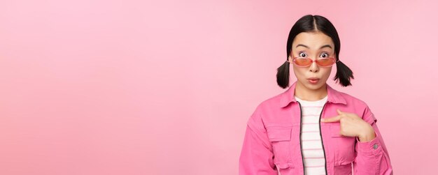 Nahaufnahme des Porträts eines asiatischen Mädchens sieht überraschte Punkte auf sich selbst aus, wobei Unglauben, ausgewählt zu werden, über rosa Hintergrund steht