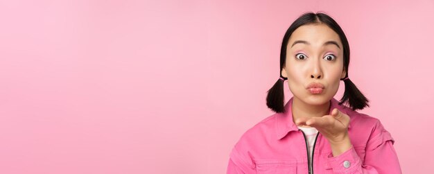 Nahaufnahme des Porträts eines schönen dummen asiatischen Mädchens, das Luftkuss mwah in die Kamera sendet und über rosa Hintergrund steht