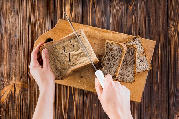 Nahaufnahme des Schnittes der Hand des Brotlaibs mit Messer auf hackendem Brett