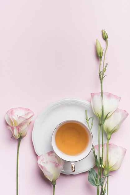 Nahaufnahme des schönen Eustoma blüht mit Tasse Tee gegen rosa Hintergrund