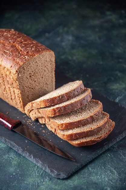 Nahaufnahme des Schwarzbrotscheibenmessers auf dunklem Farbbrett auf blauem beunruhigtem Hintergrund