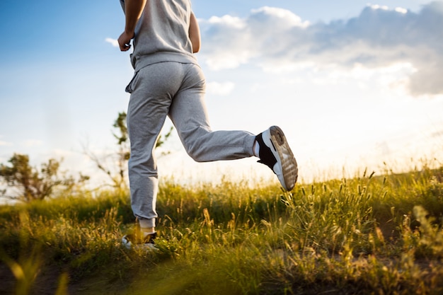 Nahaufnahme des sportlichen Mannes, der im Feld bei Sonnenaufgang joggt.