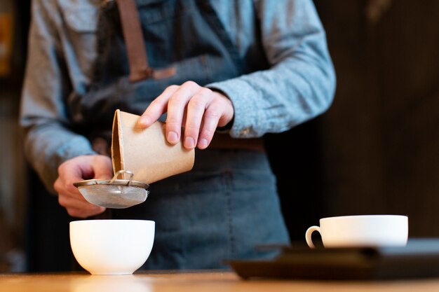 Nahaufnahme des strömenden Kaffees des Mannes in der Schale durch Sieb