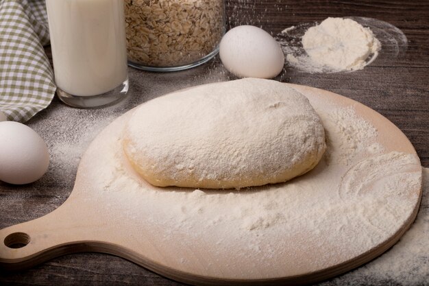 Nahaufnahme des Teigs, der mit Mehl auf Schneidebrett mit Eiern auf hölzernem Hintergrund besprüht wird