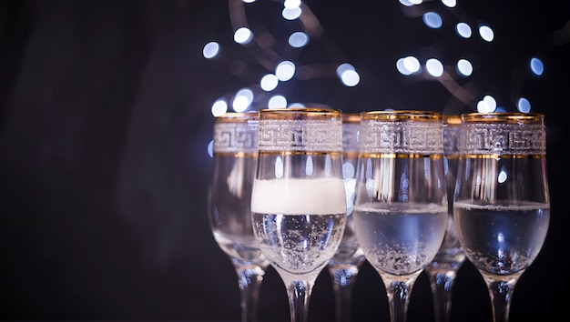 Nahaufnahme des transparenten Glases mit Champagner gegen dunklen bokeh Hintergrund
