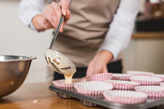 Nahaufnahme des weiblichen Bäckers gemischten Kuchenteig im Kuchenhalter gießend