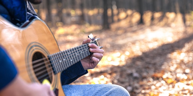 Nahaufnahme ein Mann spielt eine akustische Gitarre im Herbstwald