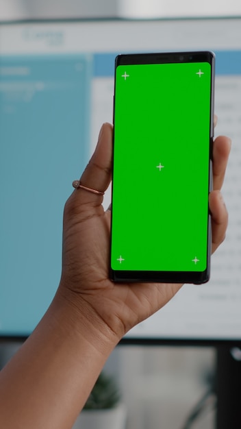 Nahaufnahme einer afrikanischen Frau, die ein Green-Screen-Chroma-Key-Telefon mit isoliertem Display in den Händen hält und eine Online-Videokonferenz-Konferenz hat. Schüler, der von zu Hause aus arbeitet, um Videos anzusehen