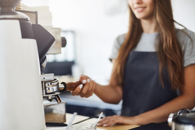 Nahaufnahme einer Barista, die an einem sonnigen Wintertag in einem hellen Café Kaffee mahlt, um eine perfekte Espressotasse zuzubereiten