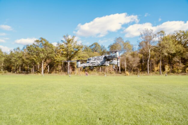 Nahaufnahme einer Drohne, die über ein grünes Feld neben einem Wald fliegt