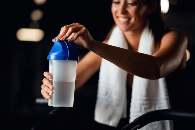 Nahaufnahme einer durstigen Sportlerin, die beim Training im Fitnesscenter einen Plastikbecher öffnet