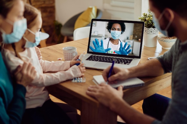 Nahaufnahme einer Familie, die während einer Coronavirus-Pandemie mit einem Arzt per Videoanruf über einen Laptop spricht