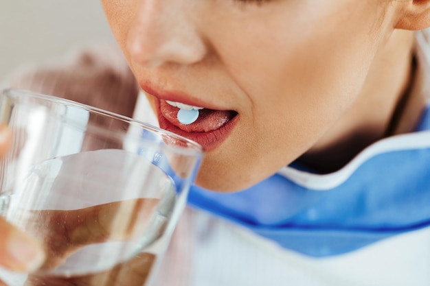 Nahaufnahme einer Frau, die ein Glas Wasser trinkt, während sie die Pille nimmt