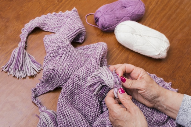 Nahaufnahme einer Frau, die purpurroten Wollschal auf hölzernem Schreibtisch strickt