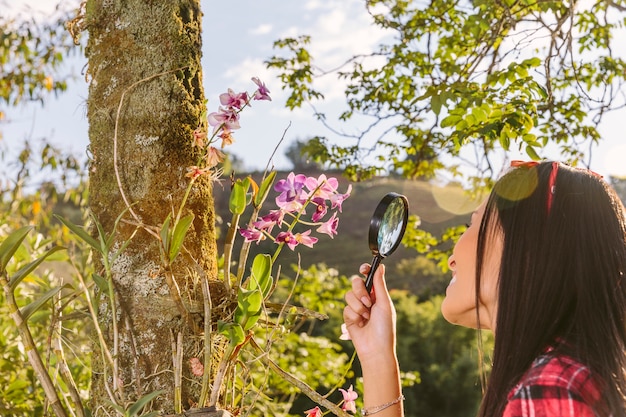 Nahaufnahme einer Frau, die rosa Blume durch Lupe betrachtet