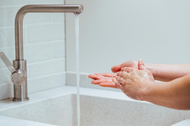 Nahaufnahme einer Frau, die sich die Hände mit Seife unter dem Waschbecken reibt