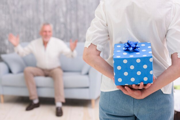 Nahaufnahme einer Frau, die zurück Geschenkbox hinter ihr versteckt, überraschend ihren Ehemann