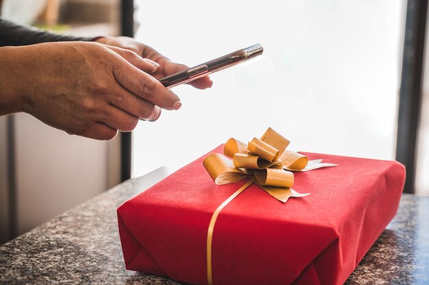 Nahaufnahme einer Frau mit einem Smartphone, das ein Bild einer roten Geschenkbox auf der Theke nimmt