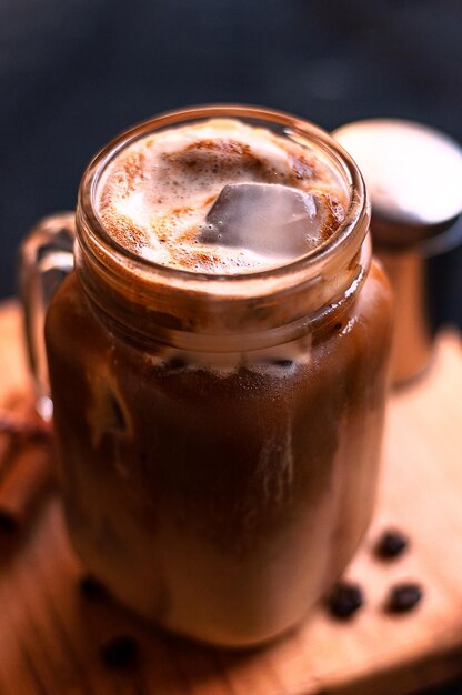 Nahaufnahme einer gefrorenen cremigen Latte-Kaffeetasse und gerösteten Bohnen auf einem Holzbrett