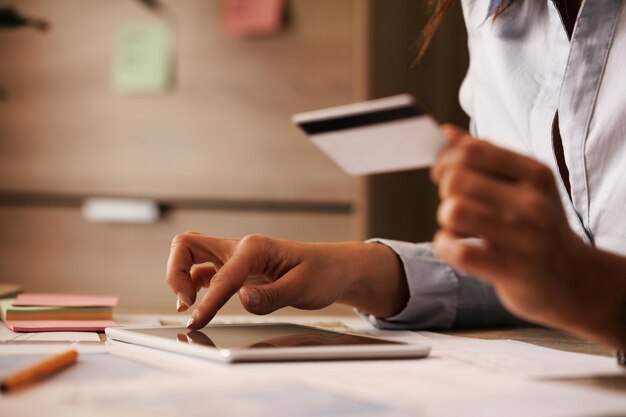 Nahaufnahme einer Geschäftsfrau, die ein digitales Tablet und eine Kreditkarte verwendet, während sie ihr Online-Bankkonto überprüft