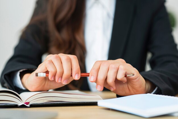 Nahaufnahme einer Geschäftsfrau, die roten Bleistift in ihren zwei Händen über dem Schreibtisch hält