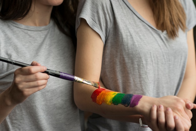 Nahaufnahme einer jungen Frau, die die lbgt Flagge über der Hand ihrer Freundin mit Malerpinsel malt
