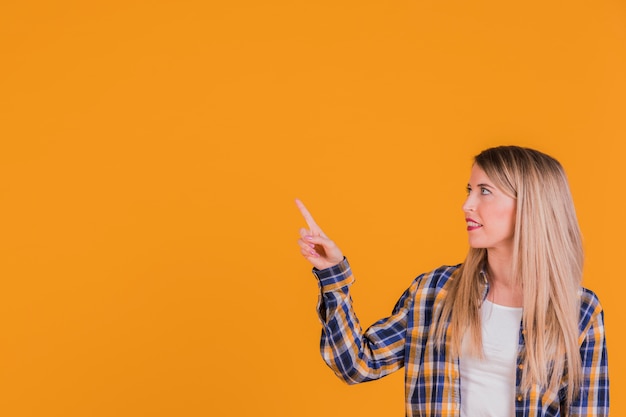 Nahaufnahme einer jungen Frau, die ihren Finger gegen einen orange Hintergrund zeigt