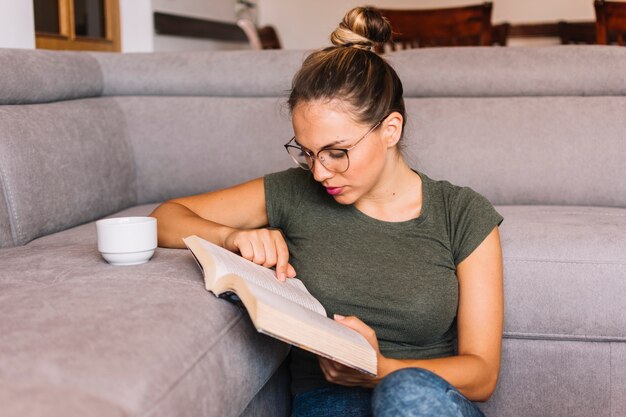 Nahaufnahme einer jungen Frau mit Tasse Kaffee auf Sofalesebuch