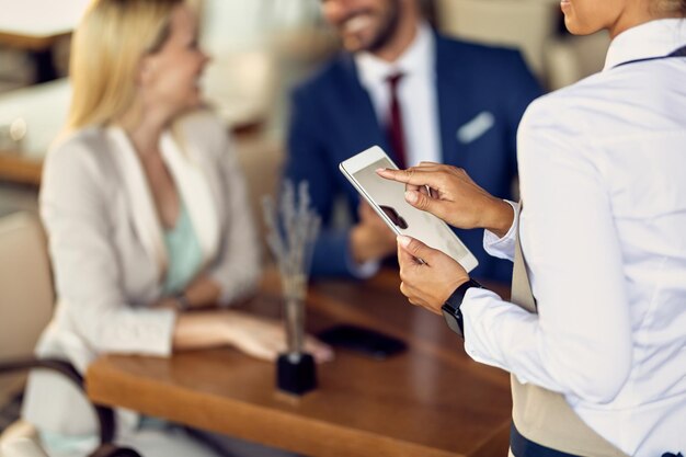 Nahaufnahme einer Kellnerin, die Touchpad verwendet, während sie in einem Café eine Bestellung entgegennimmt