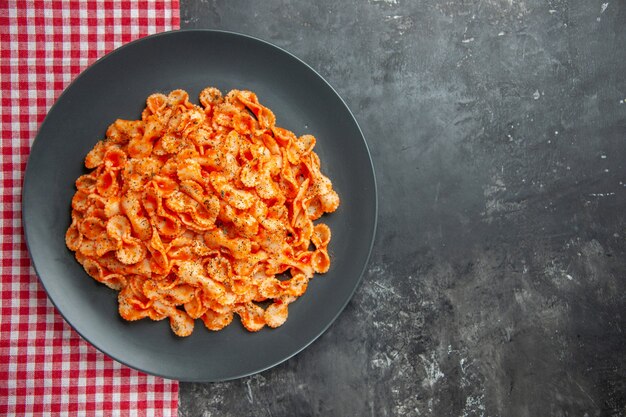 Nahaufnahme einer köstlichen Pasta-Mahlzeit auf einem schwarzen Teller zum Abendessen auf einem roten, gestreiften Handtuch auf dunklem Hintergrund