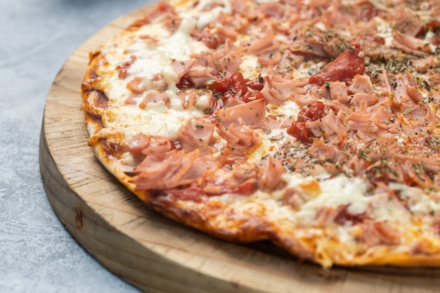 Nahaufnahme einer köstlichen Pizza mit geschnittenen Würstchen und geschmolzenem Käse auf einem Brett unter den Lichtern