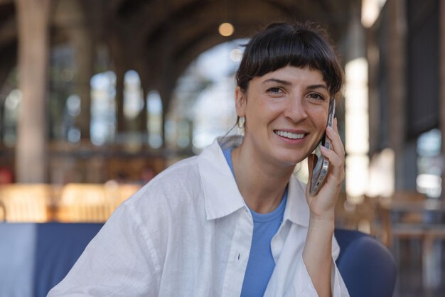 Nahaufnahme einer lächelnden Frau, die mit dem Smartphone in die Kamera blickt