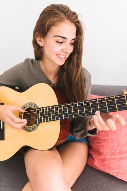 Nahaufnahme einer lächelnden Jugendlichen, die zu Hause Gitarre spielt