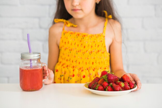 Kostenloses Foto nahaufnahme einer mädchenhalteplatte von erdbeeren und von smoothiesglas