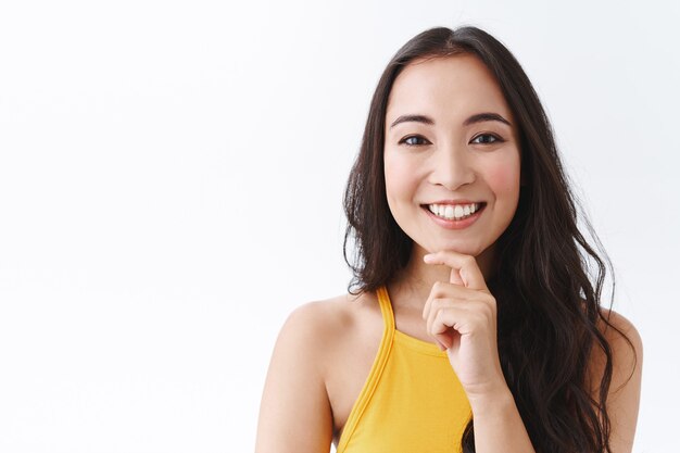 Nahaufnahme einer nachdenklichen und glücklichen jungen intelligenten ostasiatischen Unternehmerin, die neue Konzepte für ihr Geschäft ausdenkt, das Kinn nachdenklich berührt und lächelt, eine gute Idee hört, den Plan genehmigt