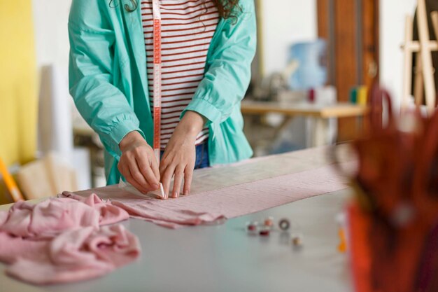 Nahaufnahme einer Näherin, die in einer modernen Nähwerkstatt mit Seife auf rosafarbenem Textil zeichnet