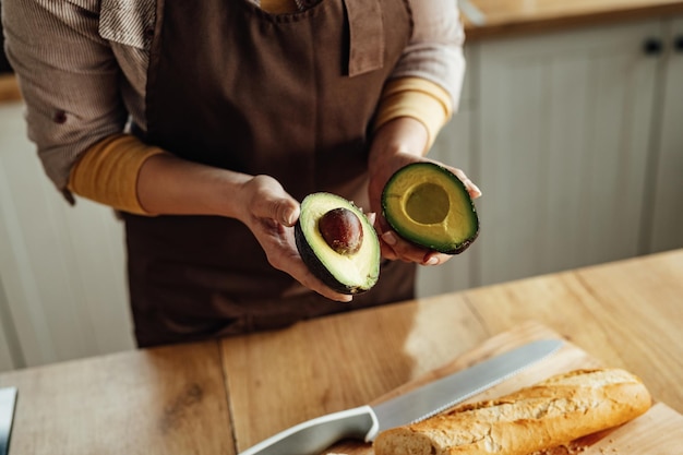 Nahaufnahme einer nicht erkennbaren Frau, die Avocado beim Zubereiten von Speisen in der Küche schält