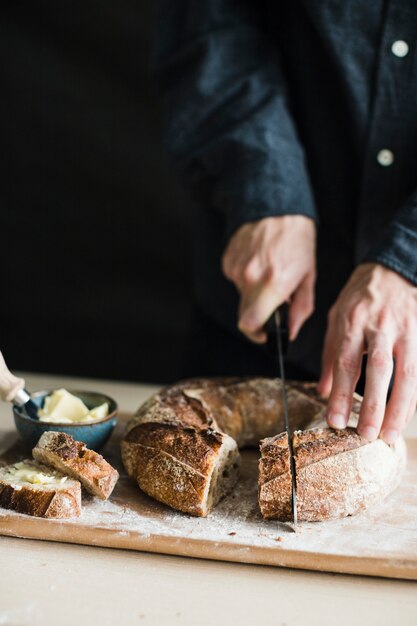 Nahaufnahme einer Person, die Bagel mit Messer auf hackendem Brett schneidet