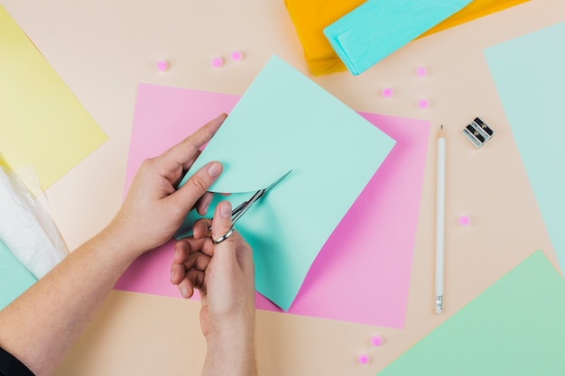 Nahaufnahme einer Person, die das Papier mit scissor auf farbigem Hintergrund schneidet