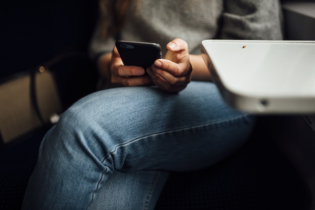 Nahaufnahme einer Person, die mit gekreuzten Beinen sitzt und ein Telefon unter den Lichtern hält