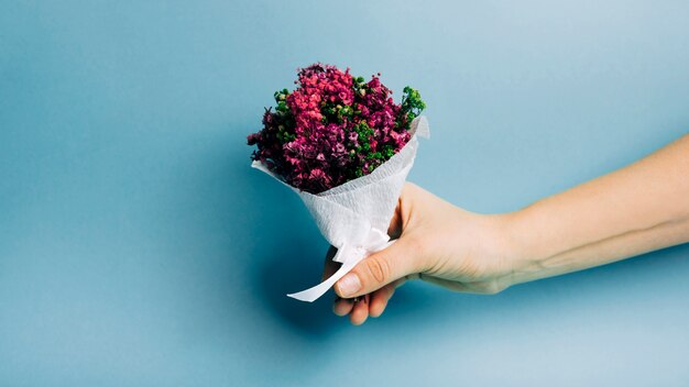 Nahaufnahme einer Personenhand, die schönen Blumenstrauß gegen blauen Hintergrund hält