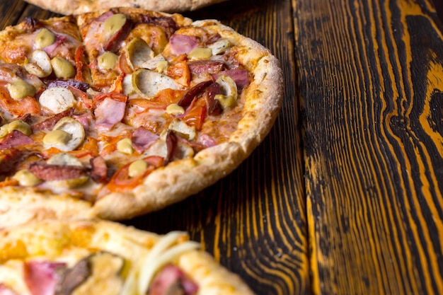 Nahaufnahme einer pizza mit schinken, tomaten, würstchen und anderen belägen und käse auf holztisch