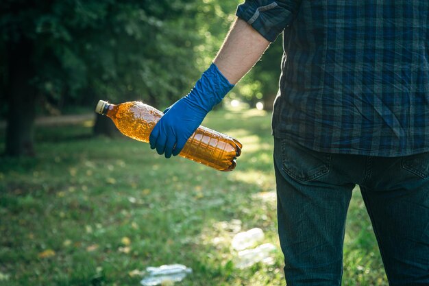 Nahaufnahme einer Plastikflasche in einer männlichen Hand, die die Natur aufräumt