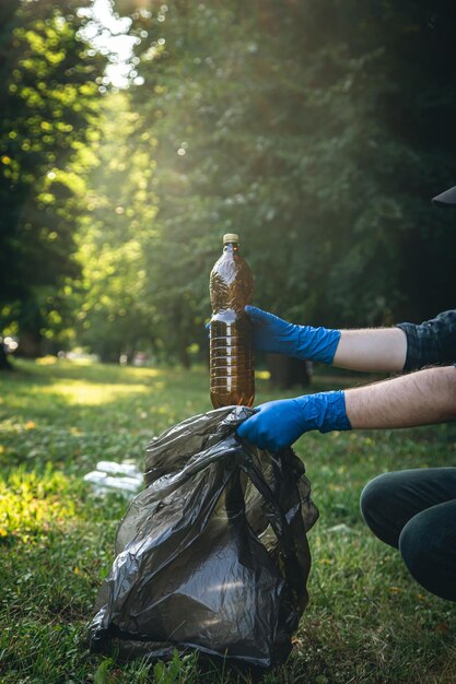 Nahaufnahme einer Plastikflasche in einer männlichen Hand, die die Natur aufräumt