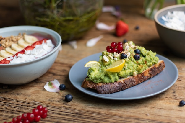 Nahaufnahme einer Scheibe Schwarzbrot mit Avocado-Nudeln und einer Smoothie-Schüssel