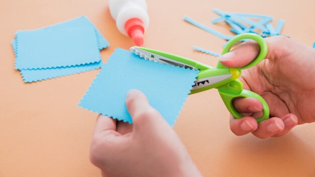 Nahaufnahme einer Schere, die das blaue Papier auf farbigem Hintergrund schneidet